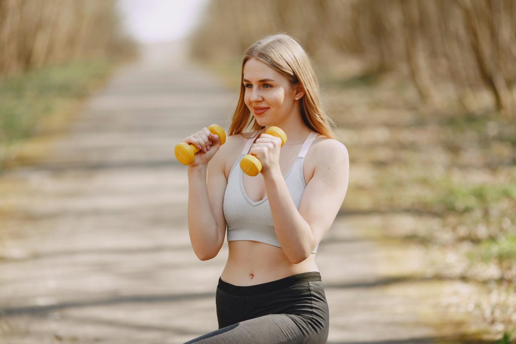 Fit woman lifting dumbbells on a sunny day, embracing a healthy outdoor workout.