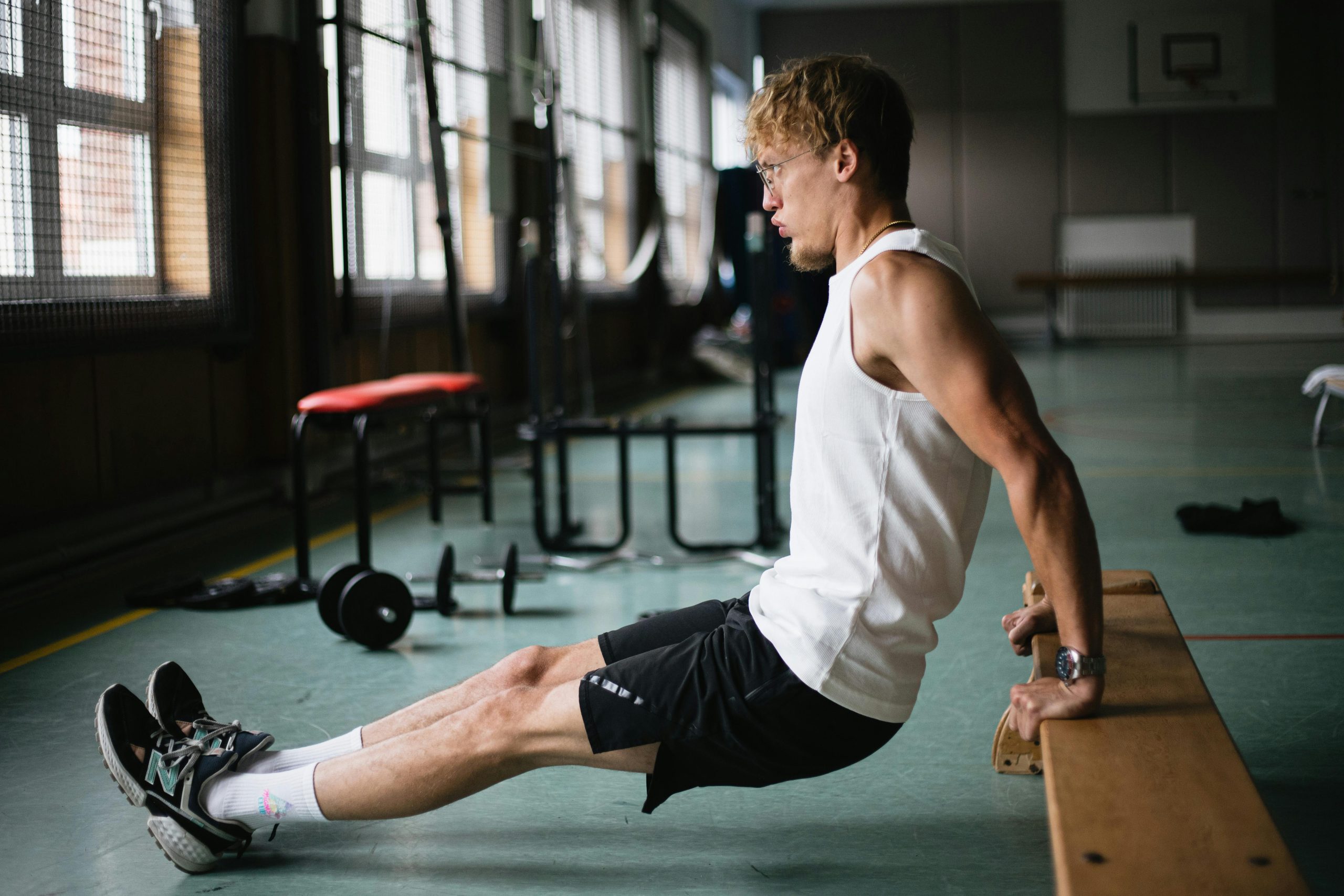 Side view of muscular sportsman in sportswear and glasses doing tricep dips exercises in gym