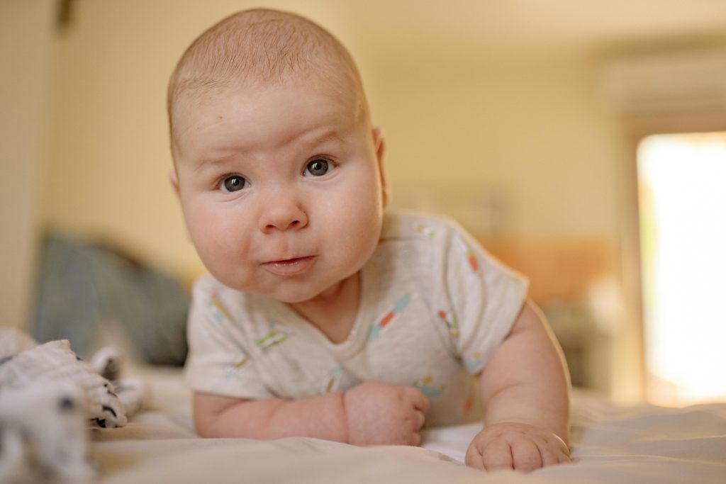 Cute baby in a onesie smiling while lying indoors. Perfect for family and parenting themes.