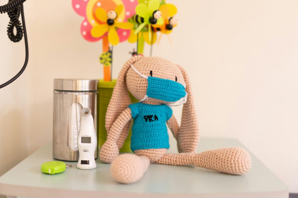 Cozy pediatric clinic decor featuring a knitted toy, digital thermometer, and cheerful flowers.