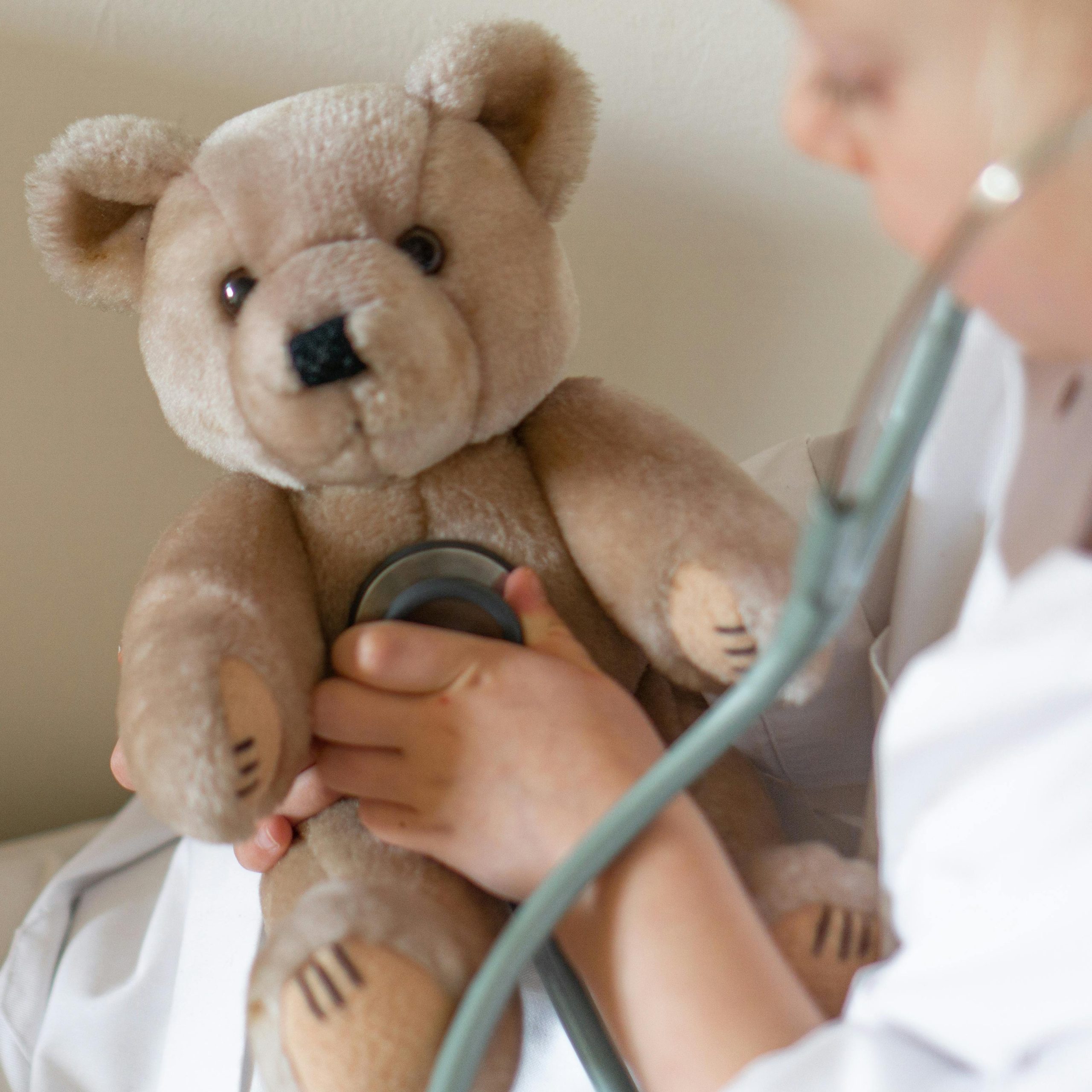 A child uses a stethoscope on a teddy bear, simulating a doctor's check-up in a playful interaction.